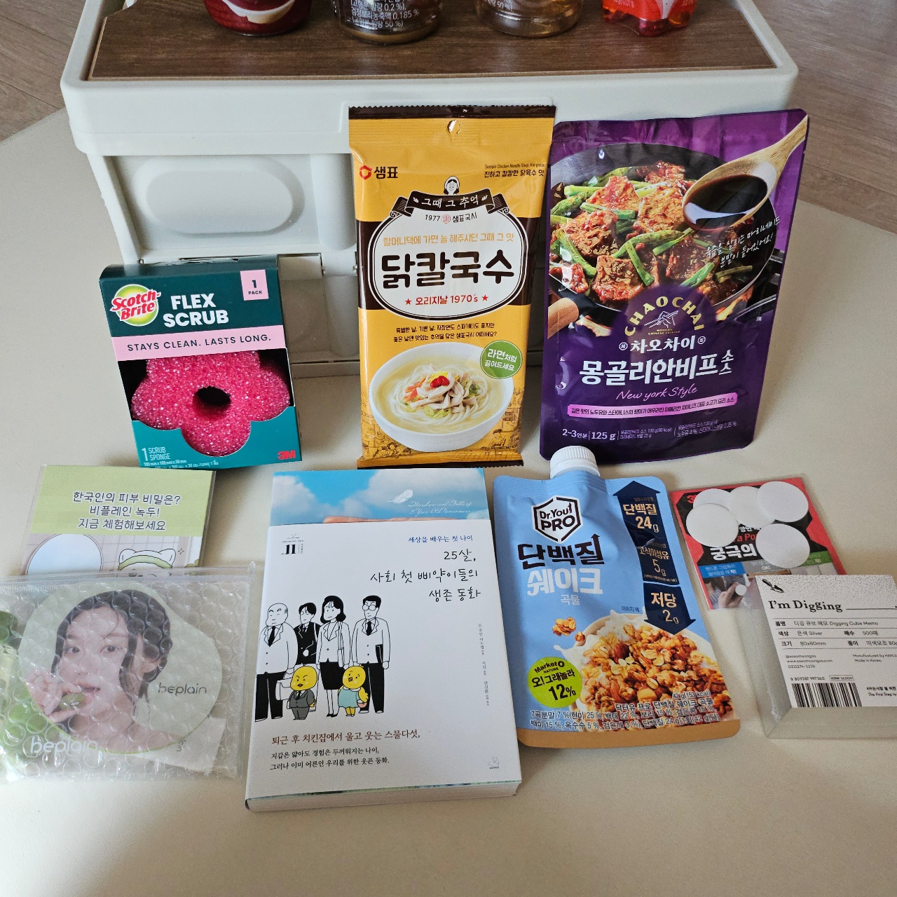 흰색 트레이에 정리된 한국 식품, 책, 스폰지, 마스크팩 등의 생활용품