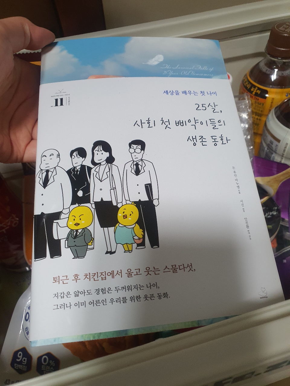 손에 들린 한국 소설책과 책상 위의 음료