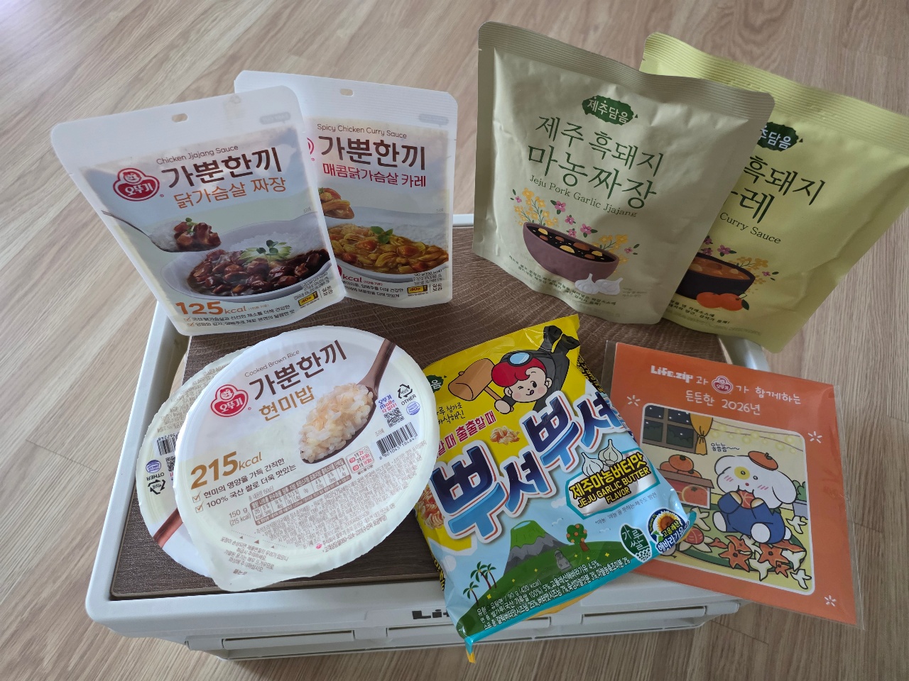 바닥에 놓인 상자 위에 정렬된 한식 소스 패키지와 밥 제품, 장난감