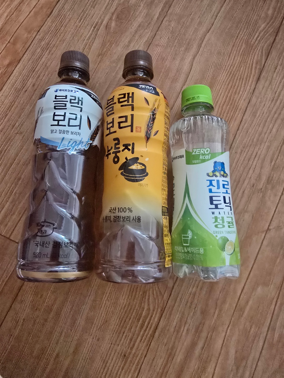 목재 바닥에 놓인 검은 콩 음료와 보리 음료, 탄산수 병