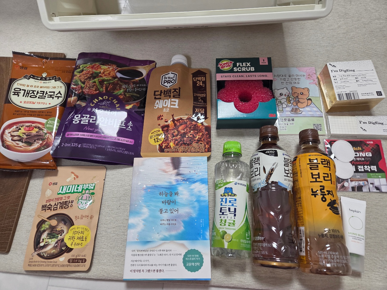 식탁에 펼쳐진 라면, 소스, 음료, 책, 생활용품 등의 물품들