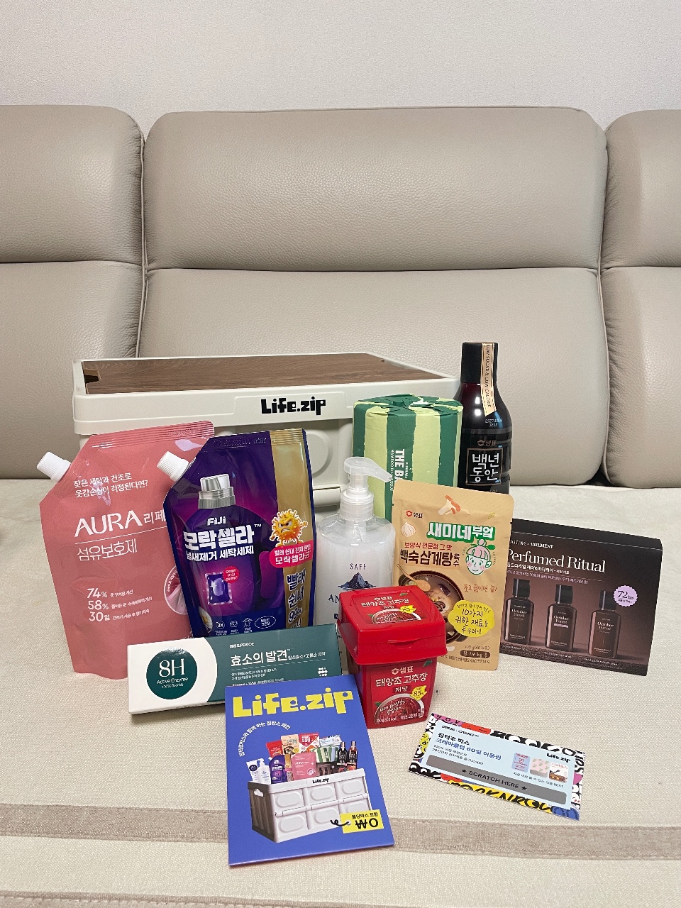 소파 앞 테이블에 전시된 화장품, 식품, 향수, 잡지 등 다양한 제품