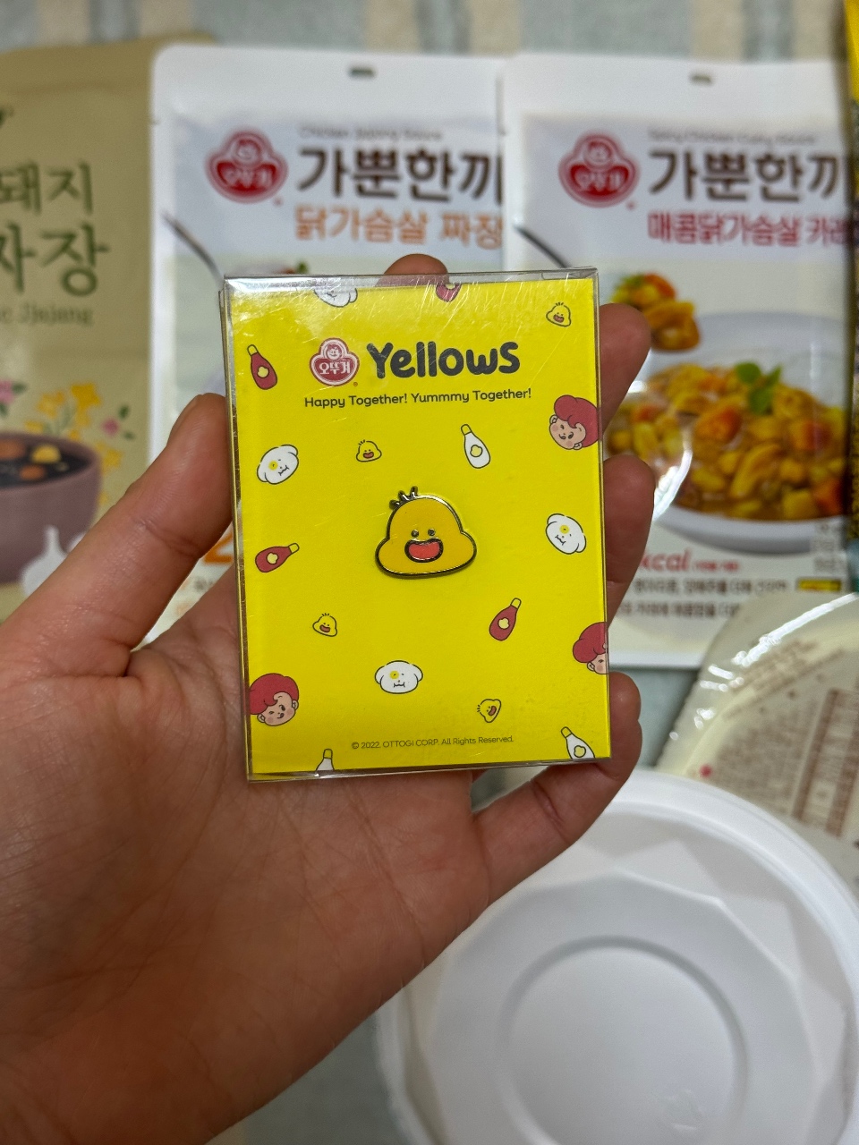 손에 들린 노란색 캐릭터 패키지와 뒤의 한식 반찬