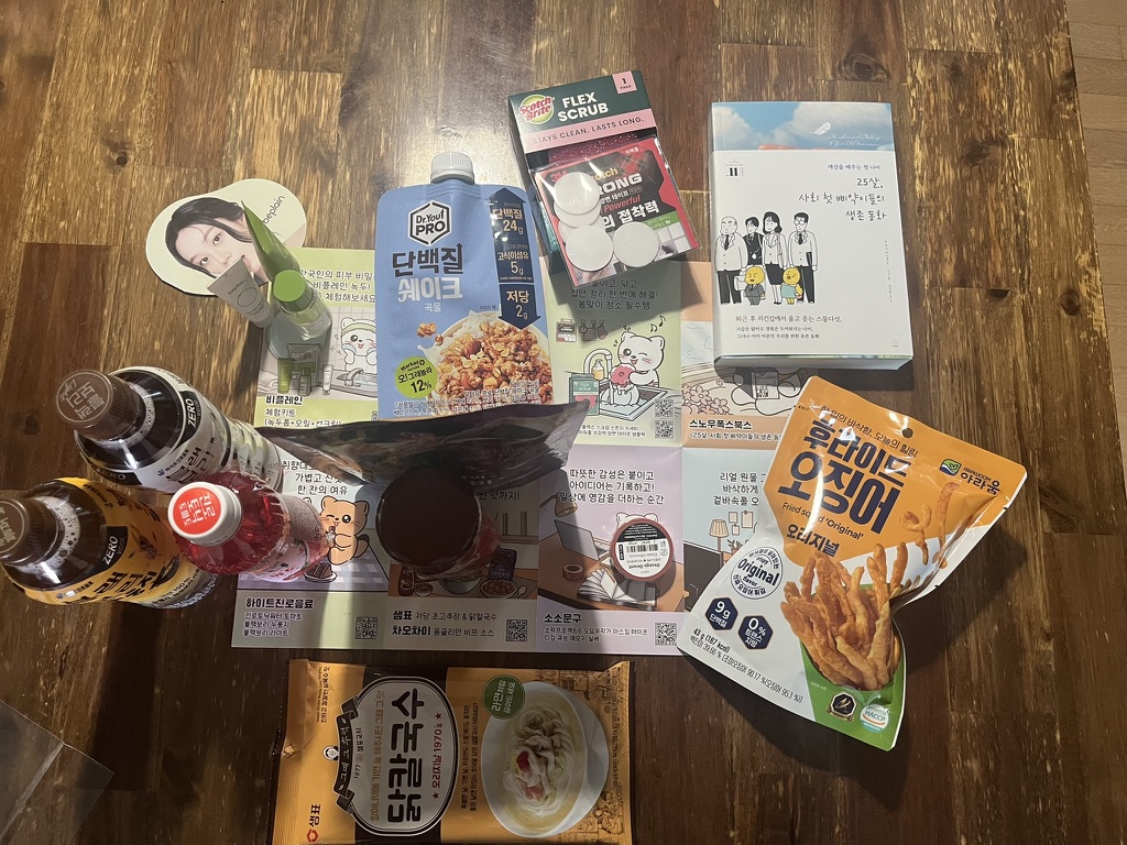 목재 바닥에 펼쳐진 한국 식품·음료·도서 제품 모음