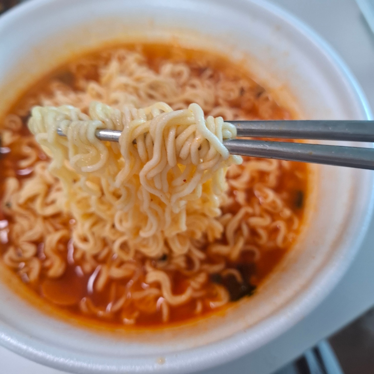젓가락으로 집은 면발과 국물이 담긴 라면