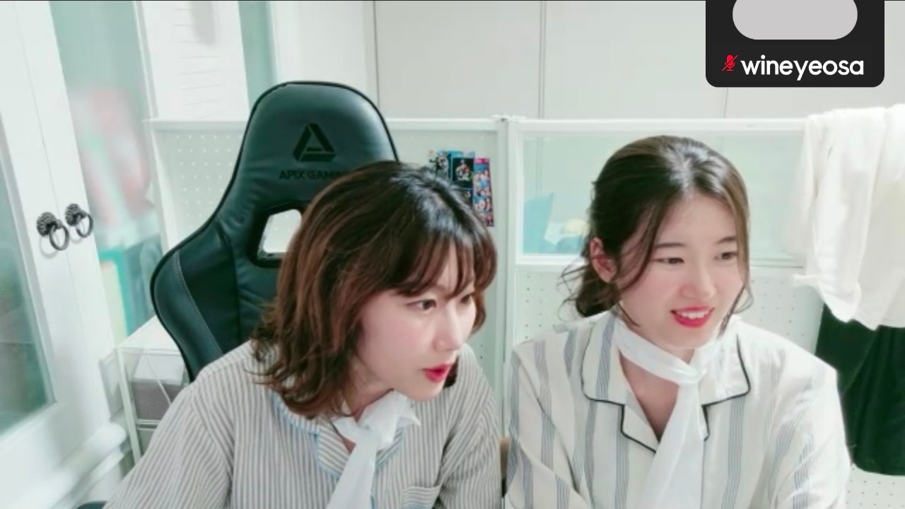게이밍 의자와 모니터가 있는 방에서 두 명이 함께 있는 모습