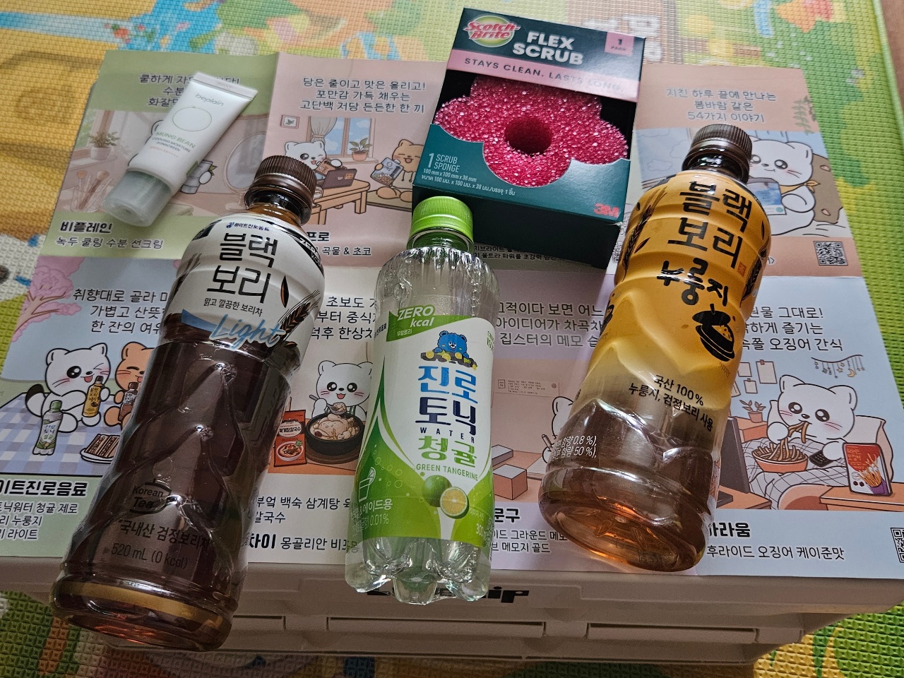 한글 라벨의 음료수 병과 스크럽 제품, 스킨케어 포장재로 구성된 한국 생활용품