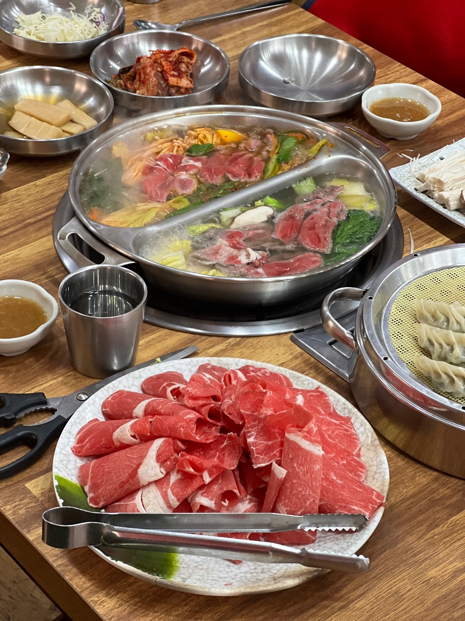 식탁에 차려진 소고기, 야채, 만두와 국물을 곁들인 샤브샤브