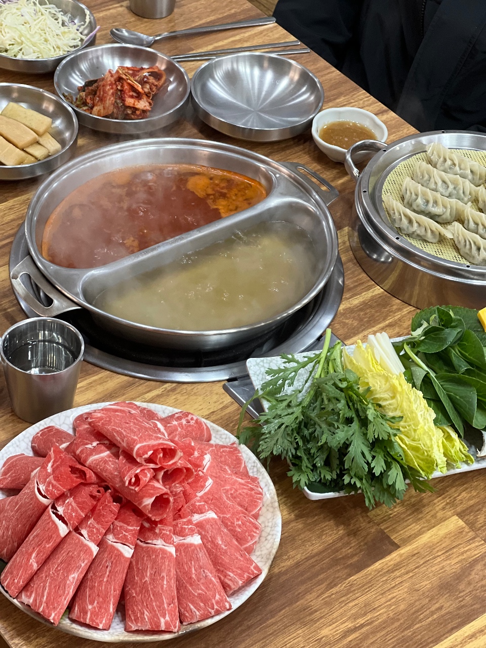 식탁에 차려진 양념육, 야채, 만두와 함께 준비된 전골 냄비