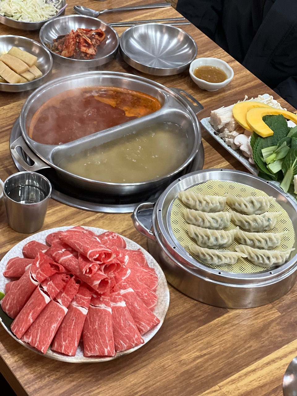 식탁에 준비된 소고기, 만두, 채소와 국물이 담긴 전골냄비