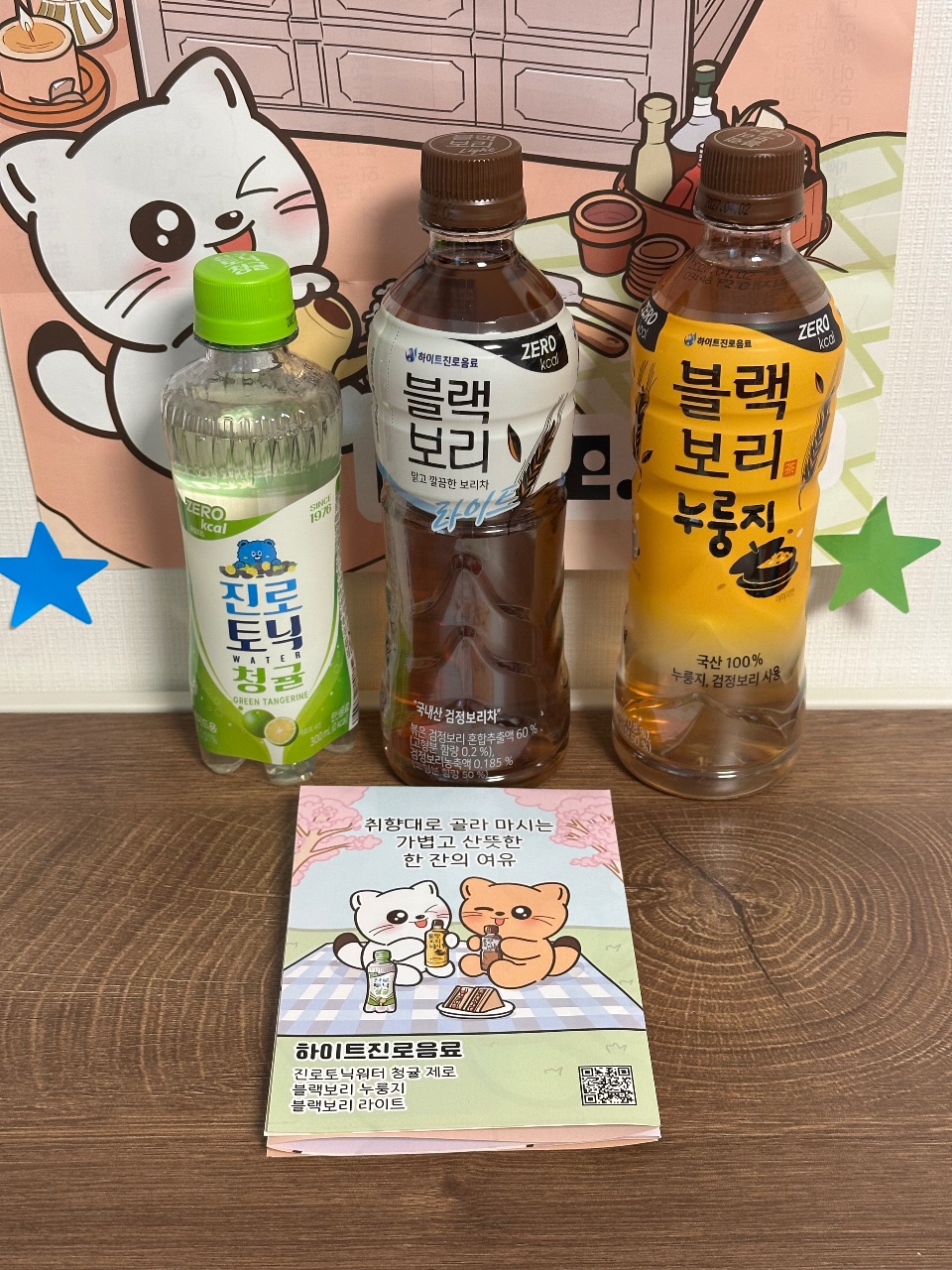 캐릭터 인형과 음료수 병, 안내 책자가 함께 놓인 제품 구성
