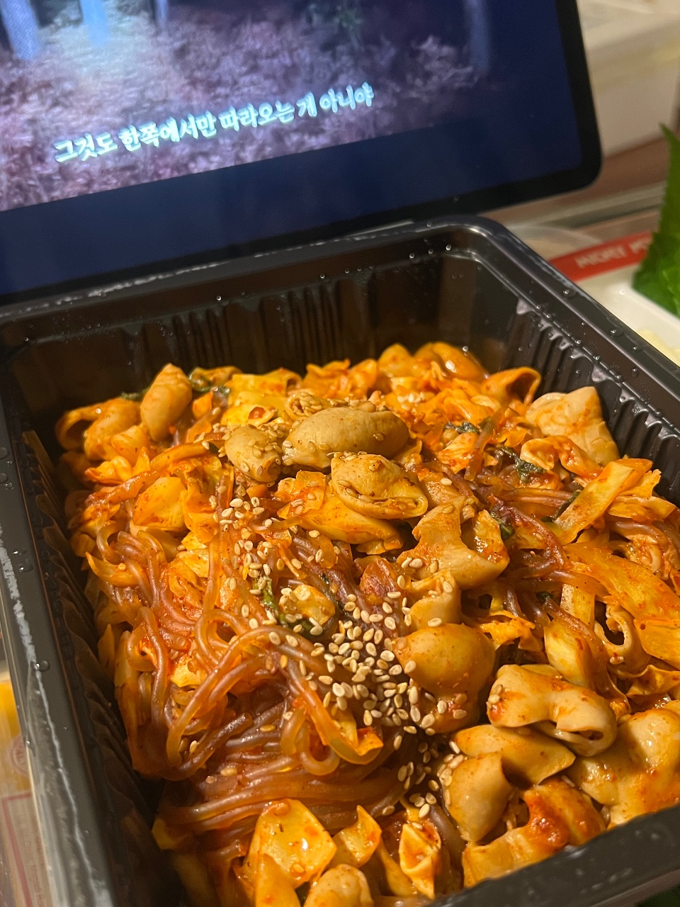 일회용 용기에 담긴 떡볶이와 닭고기, 깨가 뿌려져 있다.