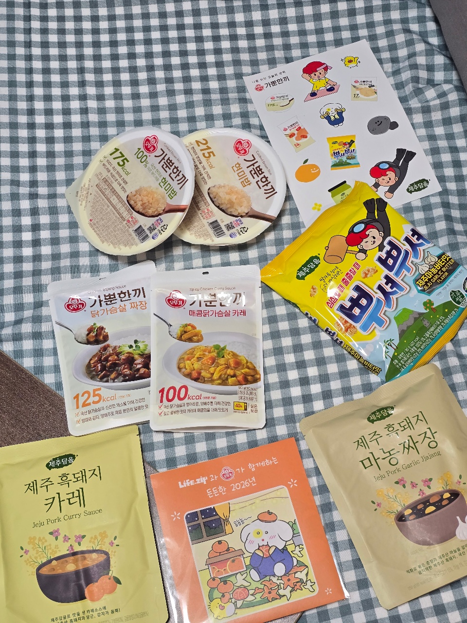 체크 천 위에 놓인 한국 레토르트 밥, 소스, 간식 패키지와 스티커
